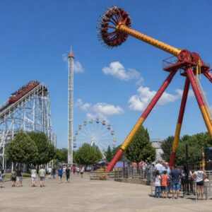 Giant pendulum frisbee ride swinging high next to a white roller coaster structure and drop tower in an outdoor amusement park