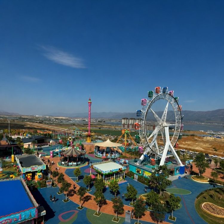 Panoramic aerial view of outdoor amusement park featuring giant ferris wheel and thrill rides under blue sky